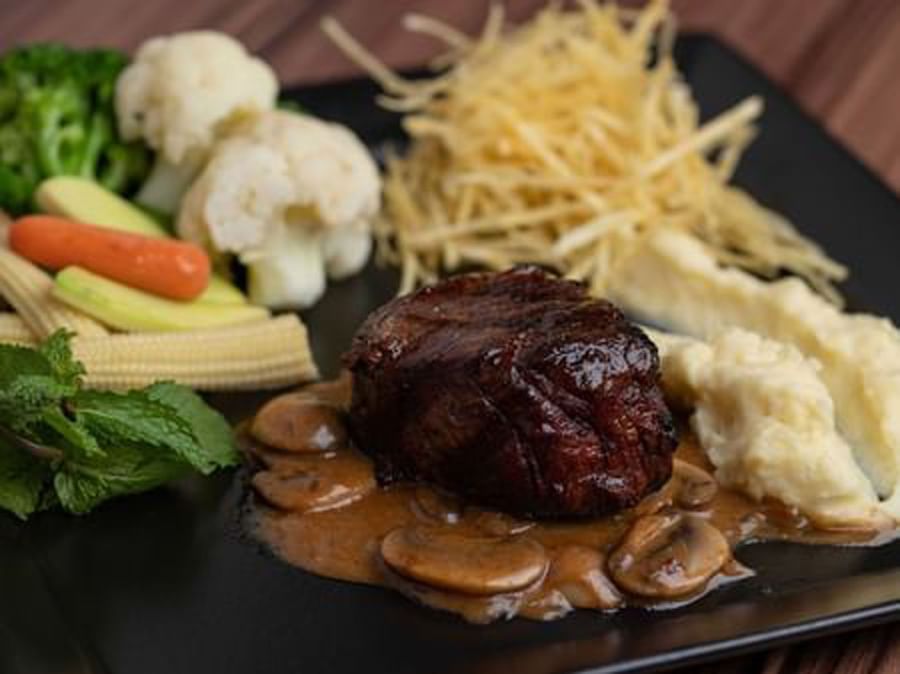 Thick steak mushroom gravy by mashed potatoes and matchstick fries on a black square plate in La Maison at Warwick Al Jubail
