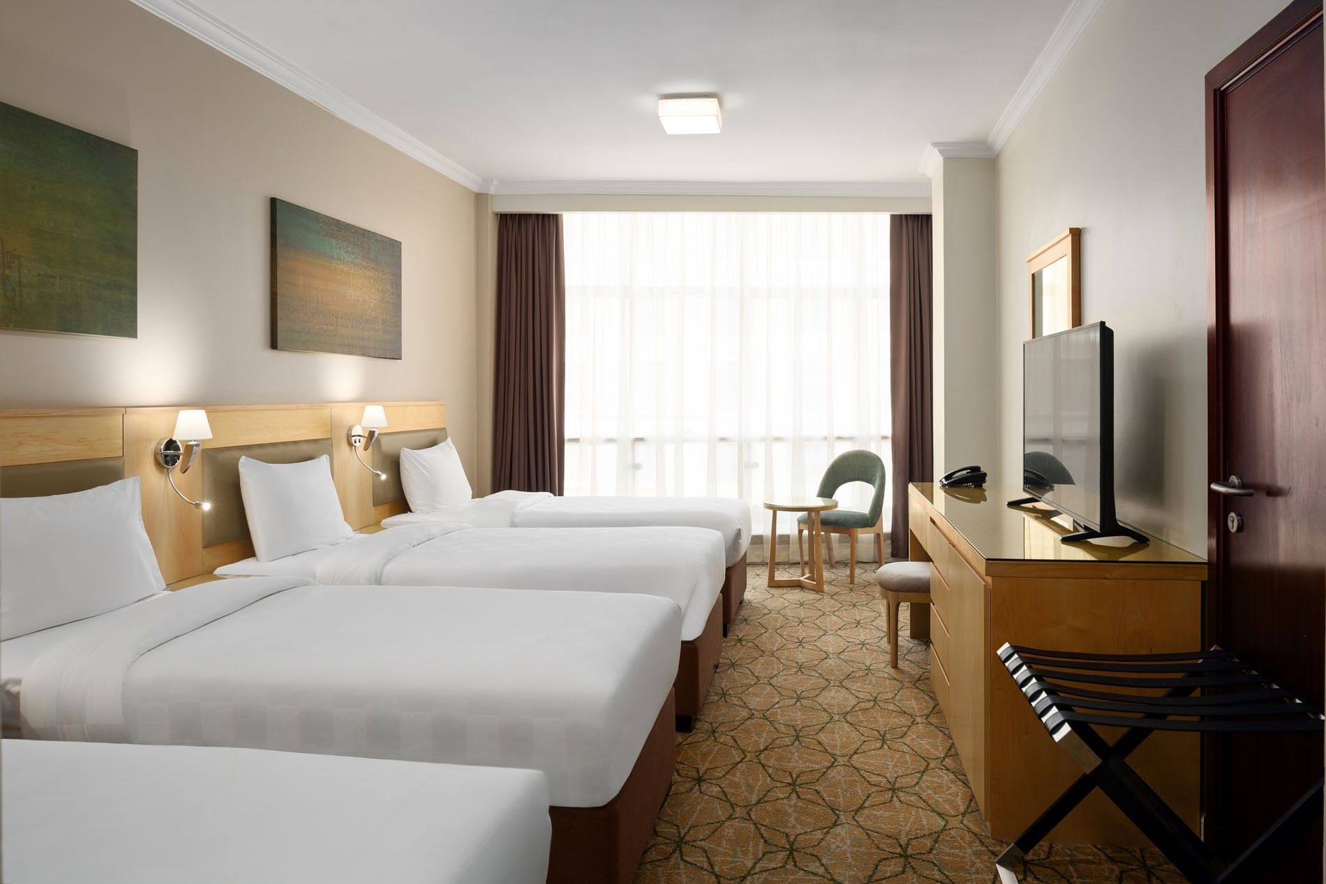 Four beds facing the TV and long wooden console with floral carpet in Standard Quadruple Room at Saja Warwick Madinah