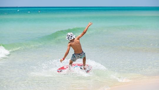 Young boy skimboarding in the sea on a sunny day near Camp Creek Inn