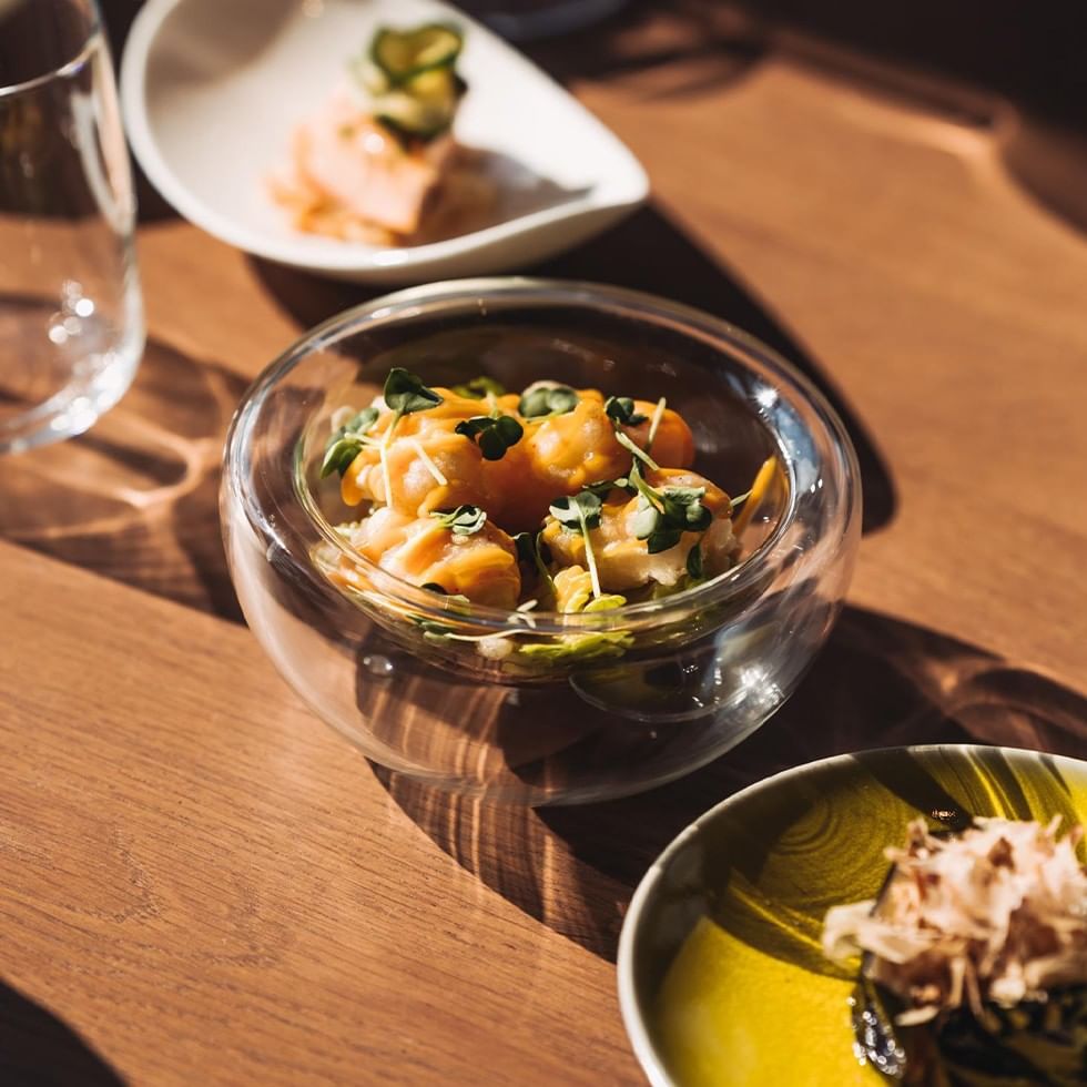 Glasteller mit Gericht, Garnitur und zwei weiteren Tellern auf einem hölzernen Tisch.