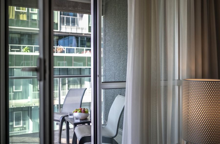 Balcony seating with chairs & a fruit bowl, seen through a glass door in Junior Balcony Suite at Warwick Le Crystal Montreal