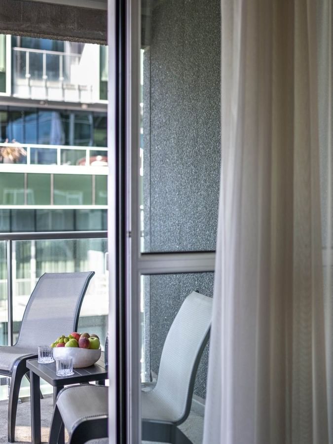 Balcony seating with chairs & a fruit bowl, seen through a glass door in Junior Balcony Suite at Warwick Le Crystal Montreal
