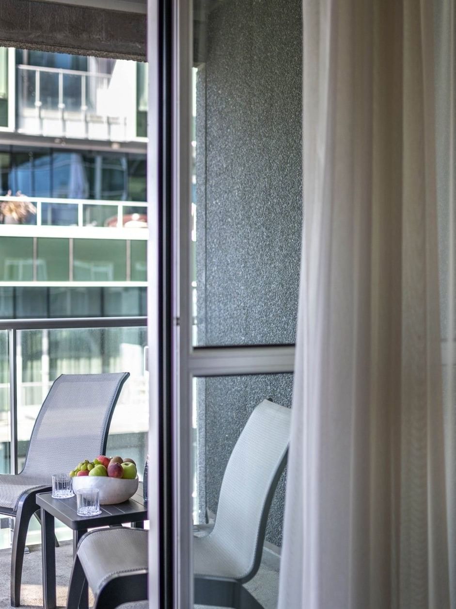 Balcony seating with chairs & a fruit bowl, seen through a glass door in Junior Balcony Suite at Warwick Le Crystal Montreal
