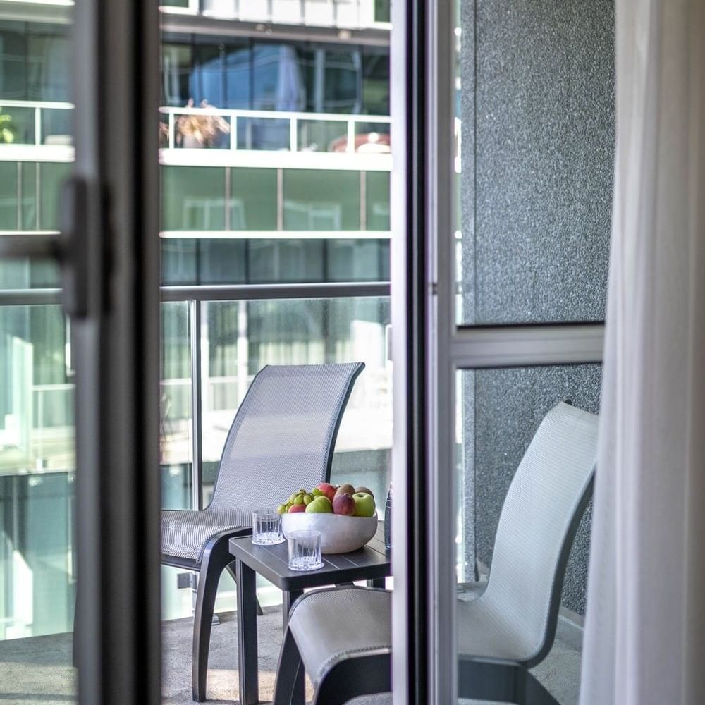 Balcony seating with chairs & a fruit bowl, seen through a glass door in Junior Balcony Suite at Warwick Le Crystal Montreal