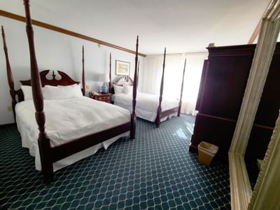 Guest bedroom with two wooden four poster beds dressed in white linens on blue patterned carpet at Avon Old Farms Hotel