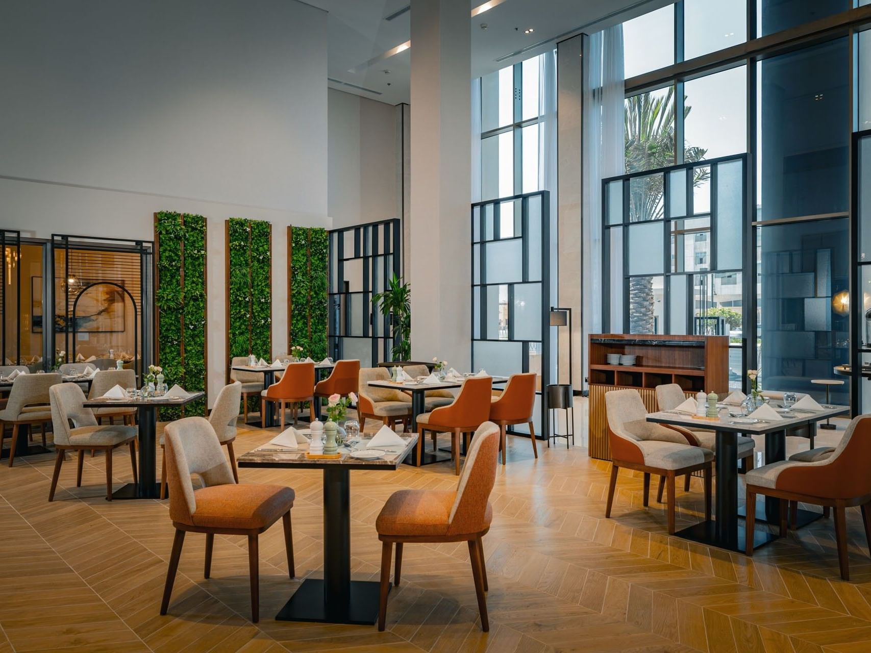 A modern, well-lit restaurant with glass walls, wooden floors, and tables set with white napkins and glasses.