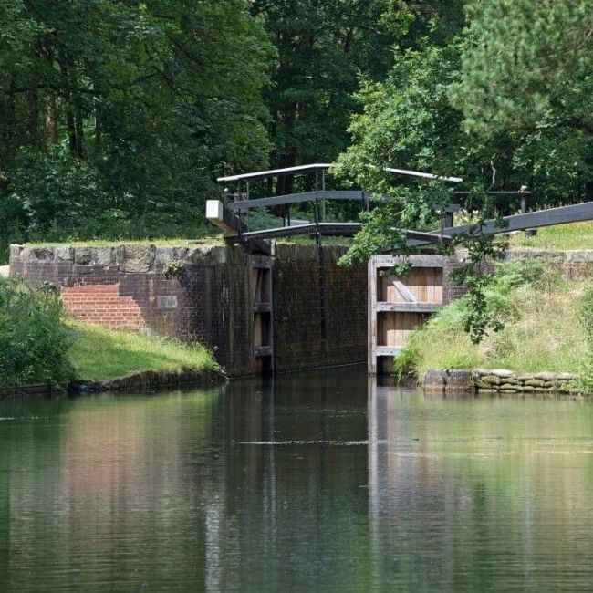 Historic Basingstoke canal lock with brick and timber gates surrounded by lush greenery along the Basingstoke Canal Waterway