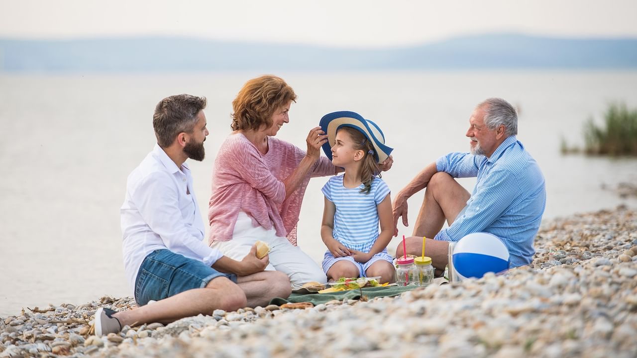 A family of four sits on a beach, enjoying a picnic with a sea view.