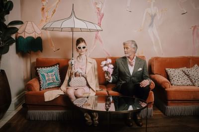 Stylish couple sits on an orange sofa, surrounded by art, floral decor, and a glass coffee table at Hotel Motto Vienna