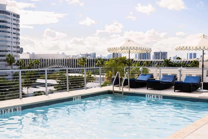 Rooftop pool at Riviera Hotel South Beach featuring blue lounge chairs under white umbrellas with a scenic city view
