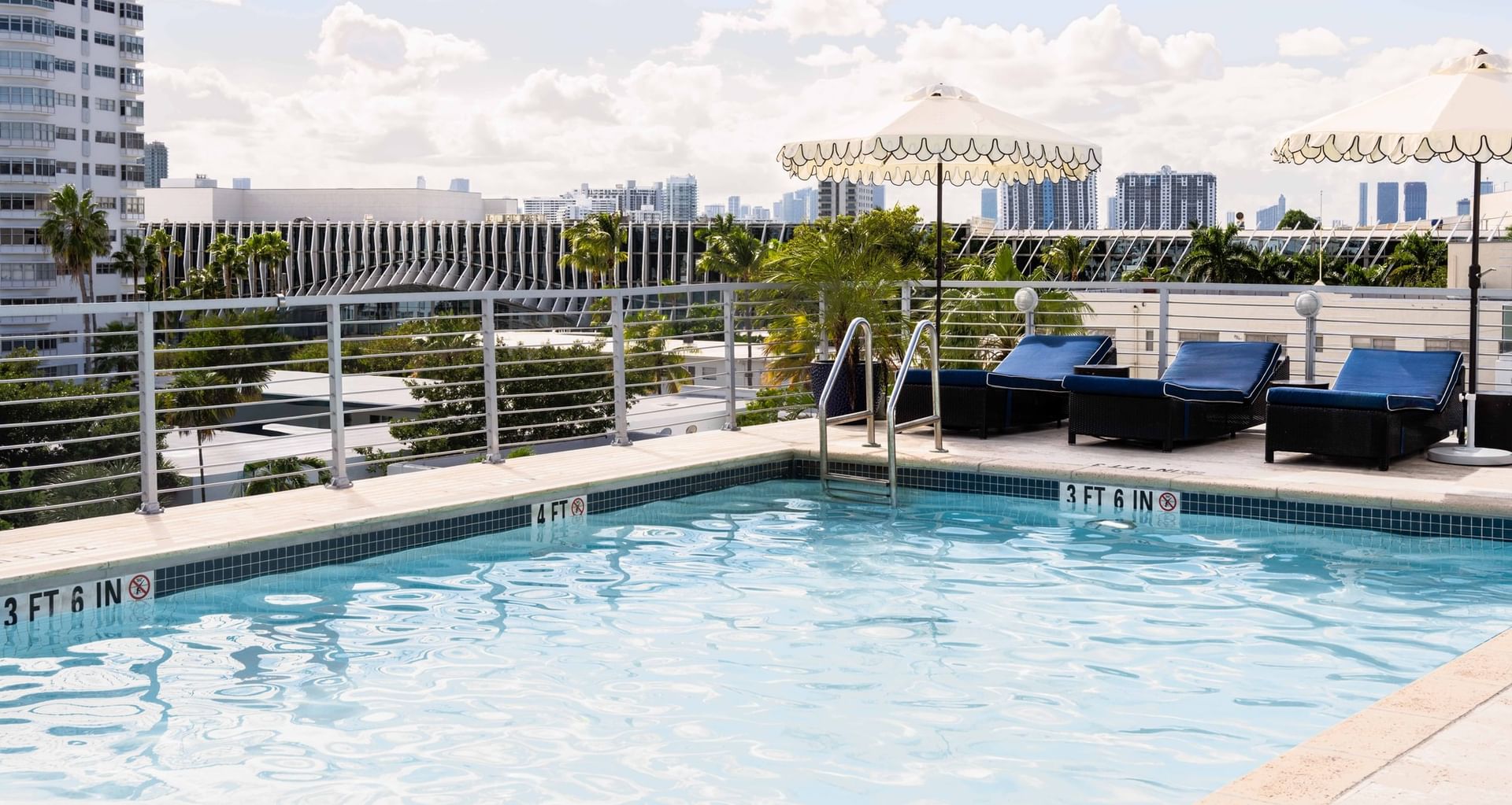 A rooftop pool with lounge chairs and umbrellas, overlooking the city skyline.