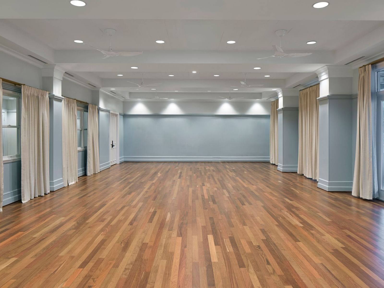 Empty Mockingbird Room with hardwood floors, blue walls, and tall draped windows at Inn at Celebration