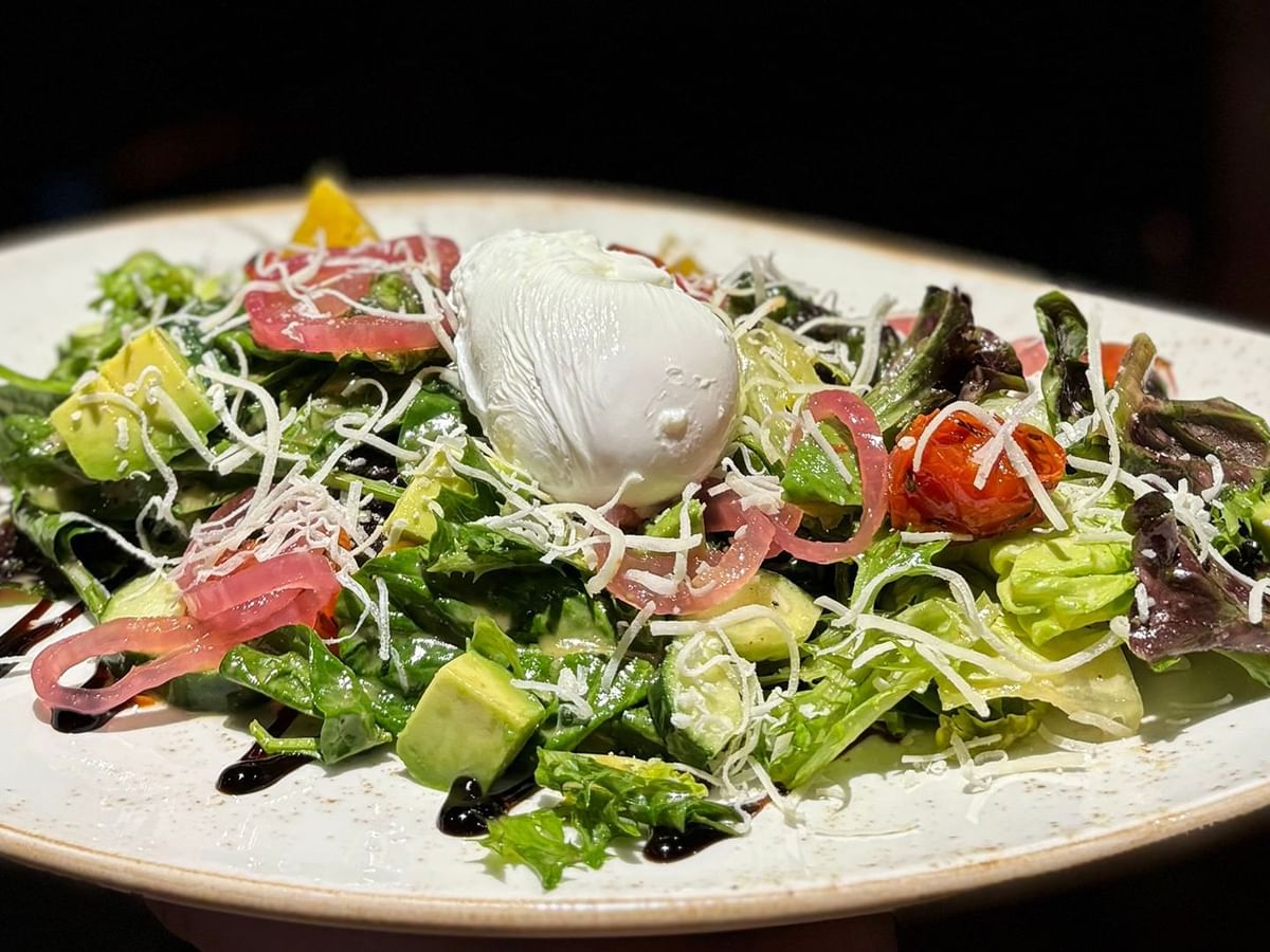 A white plate with a salad topped with avocado, burrata, and drizzled with balsamic reduction.