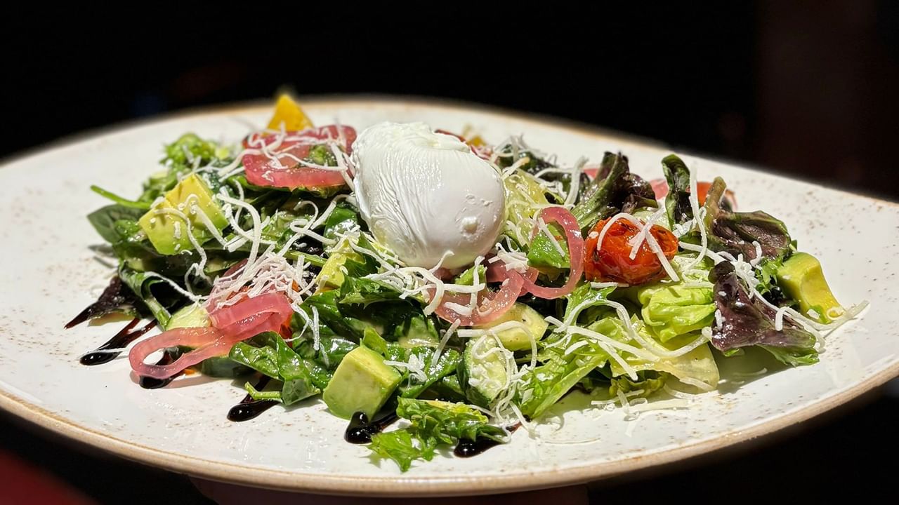 A white plate with a salad topped with avocado, burrata, and drizzled with balsamic reduction.