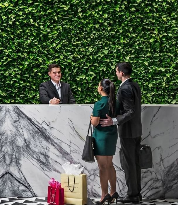 Couple checking in at marble reception desk with lush green plant wall background at Hotel X Toronto lobby area