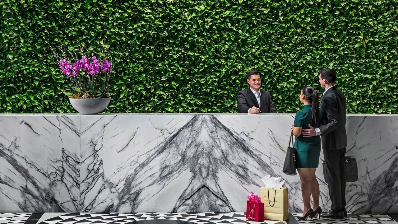 Couple checking in at marble reception desk with lush green plant wall background at Hotel X Toronto lobby area