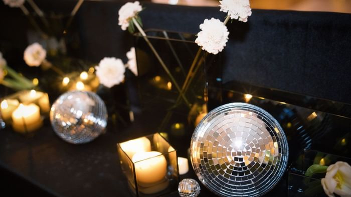 Flowers, candles, and disco balls on a table set for New Year's Eve celebration.