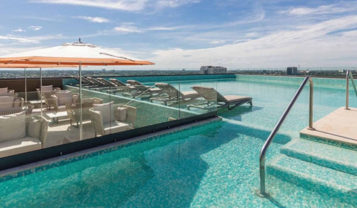 Piscina infinita en la azotea con tumbonas y sombrillas en Camino Real Hotels