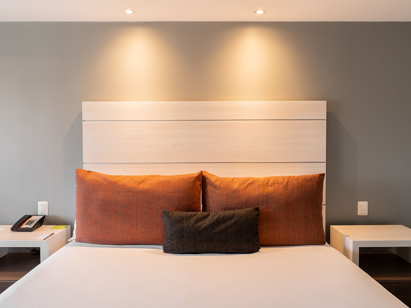 King Deluxe Room with a bed, orange pillows, and a light wood headboard under warm spotlights at Real Inn Tijuana