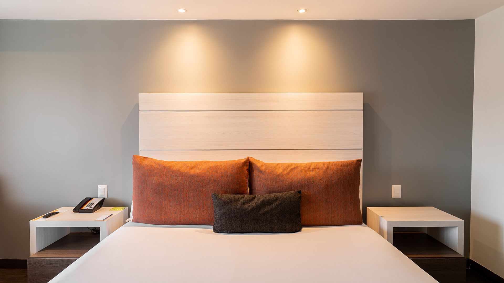 King Deluxe Room with a bed, orange pillows, and a light wood headboard under warm spotlights at Real Inn Tijuana