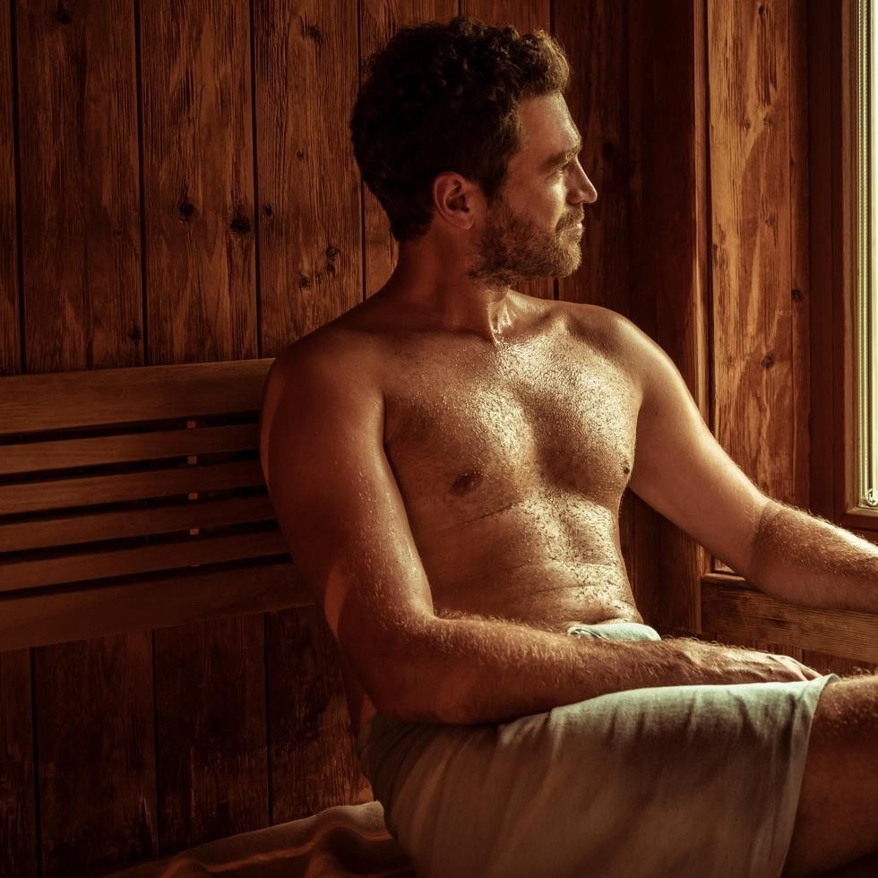 Sweating man sitting on a wooden bench in a sauna by a bright window under soft light at Falkensteiner Hotels & Residences