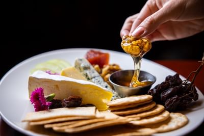 A hand drizzles honey over a beautifully arranged cheese platter at the Royal on the Park Hotel