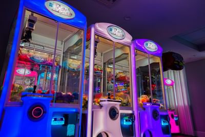 Brightly lit claw machines in blue and purple with stuffed animals inside the resort arcade at Centennial Plaza Resort