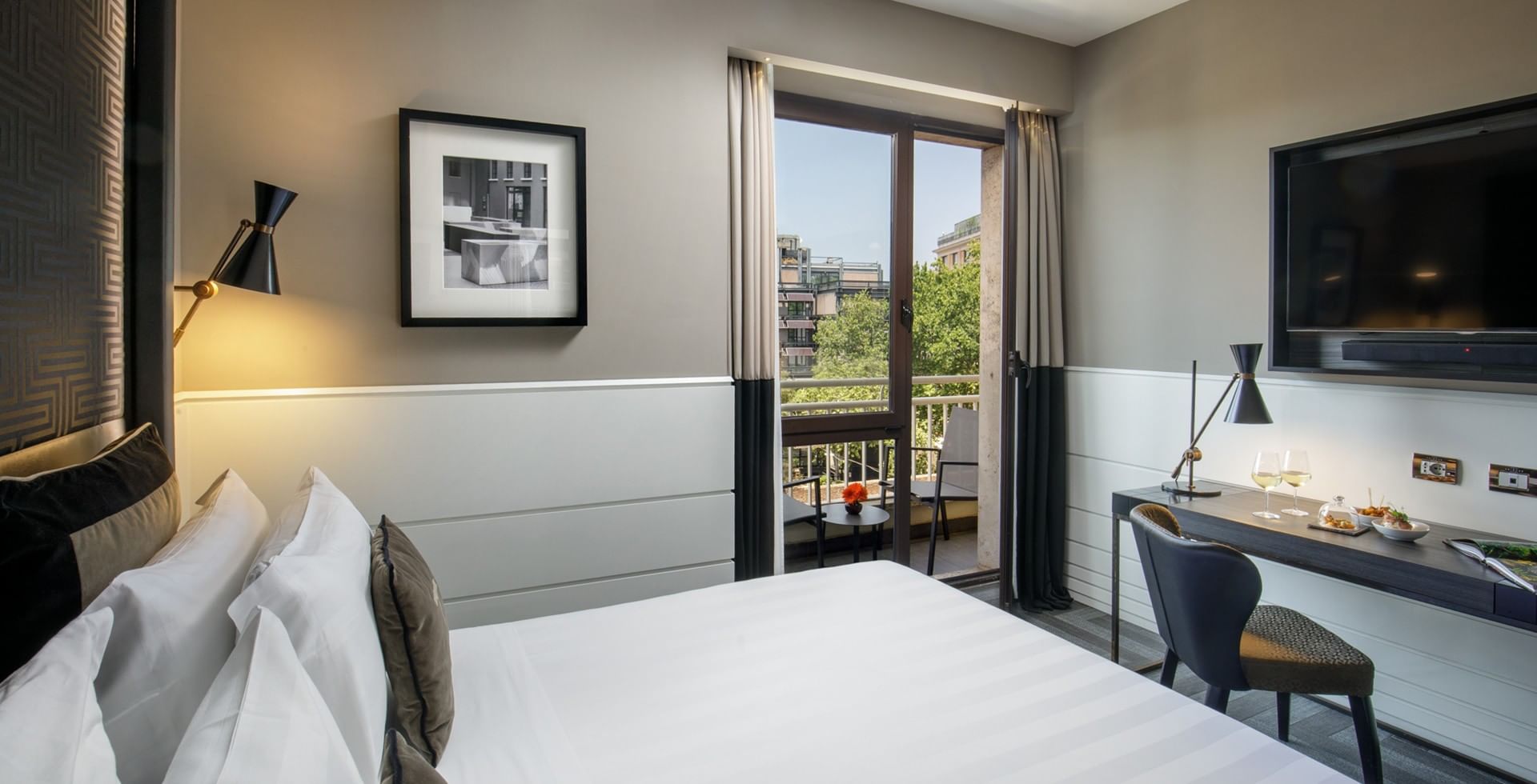 King Bed Deluxe room at Tribune Hotel Rome with elegant modern décor, spacious bed, work desk, flat-screen TV, and balcony with city views.