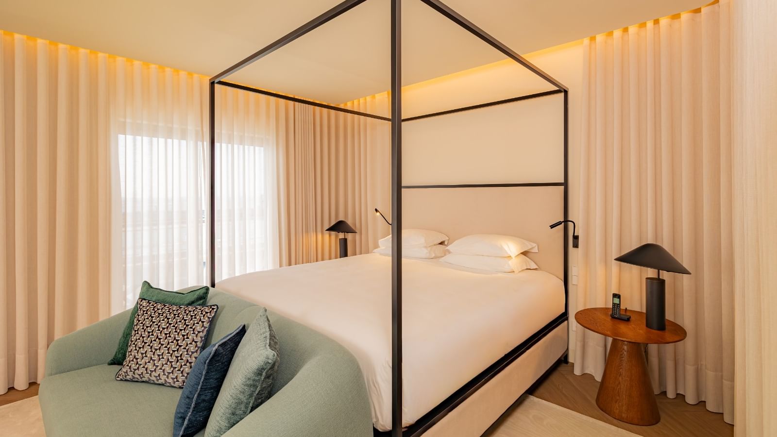 Quarto com cama de dossel, sofá, mesa de cabeceira e cortinas brancas.