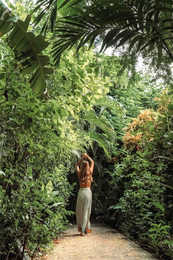 Woman walks through lush jungle gardens surrounded by vibrant green tropical palm at Cala Luna Boutique Hotel