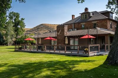 Outdoor patio deck with red umbrellas at the lodge building in Ranch at Ucross overlooking a green lawn