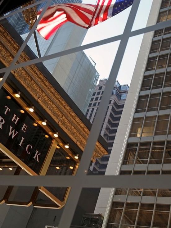 Hotel signage by an American flag under a white grid window near skyscrapers at Warwick San Francisco