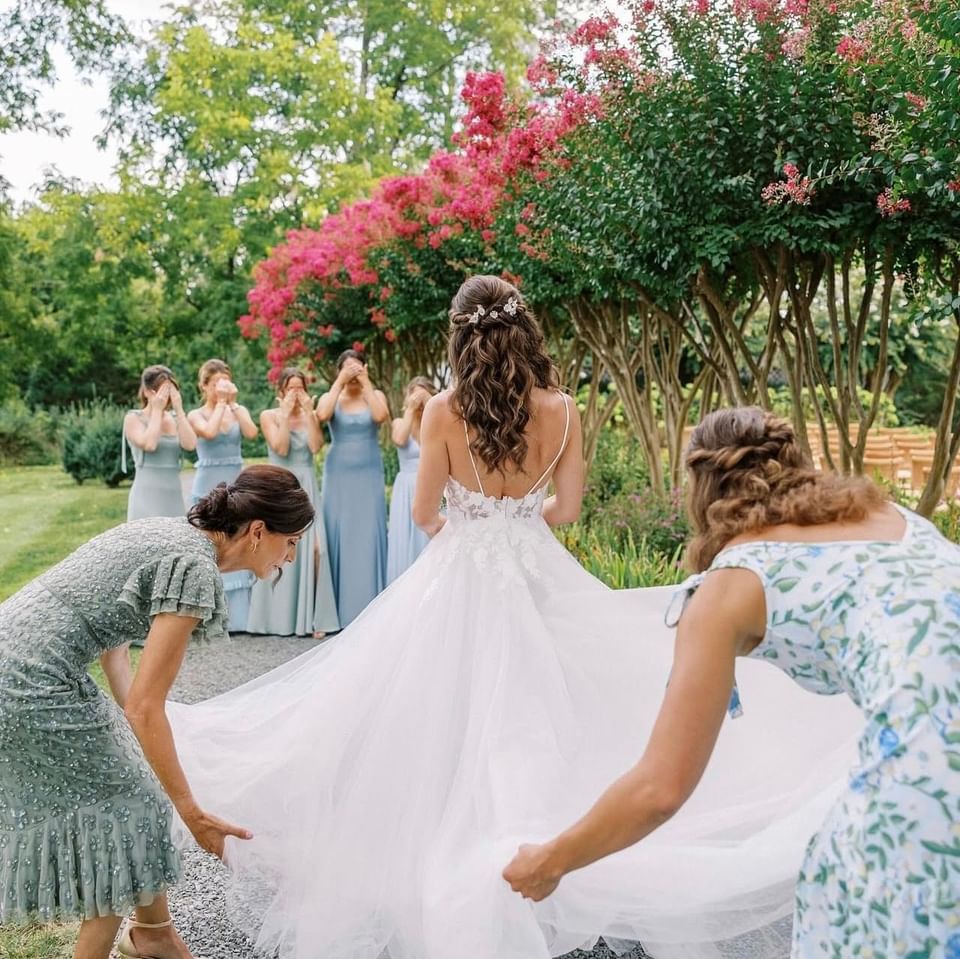Bridesmaids in blue dresses adjust the bride's white gown at the garden of The Clifton Hotel in Charlottesville, VA.