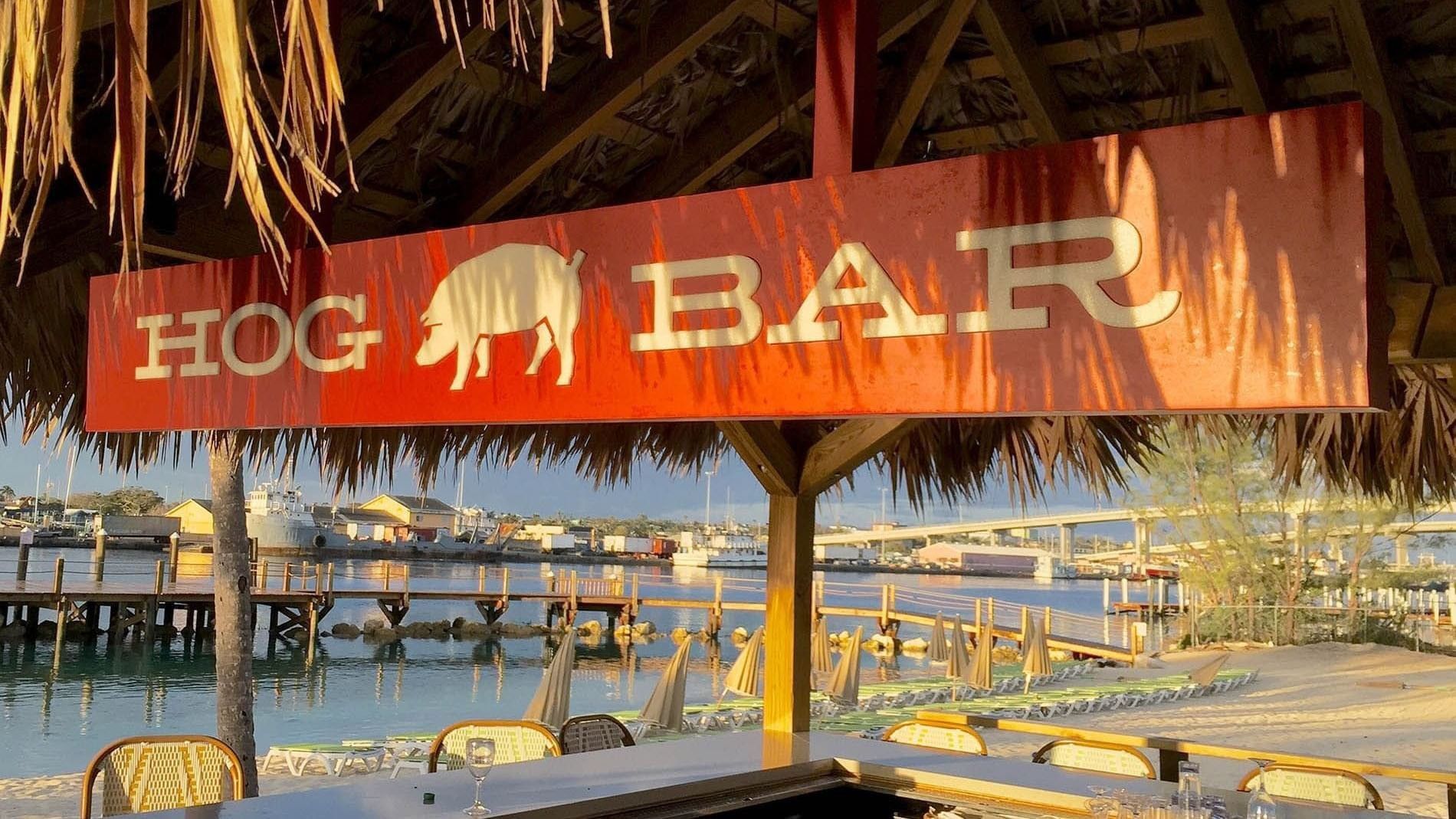 Hog Bar sign under a thatched roof by a calm bay and wooden pier at Warwick Paradise Island Bahamas