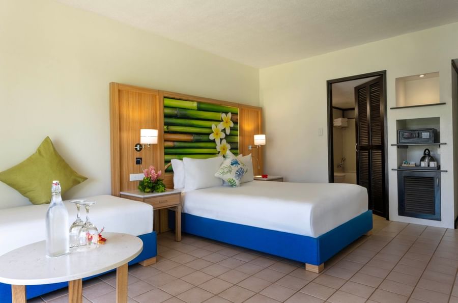 Water bottle on a table by a blue bed base under a tropical bamboo mural in Garden View Room at The Naviti Resort - Fiji
