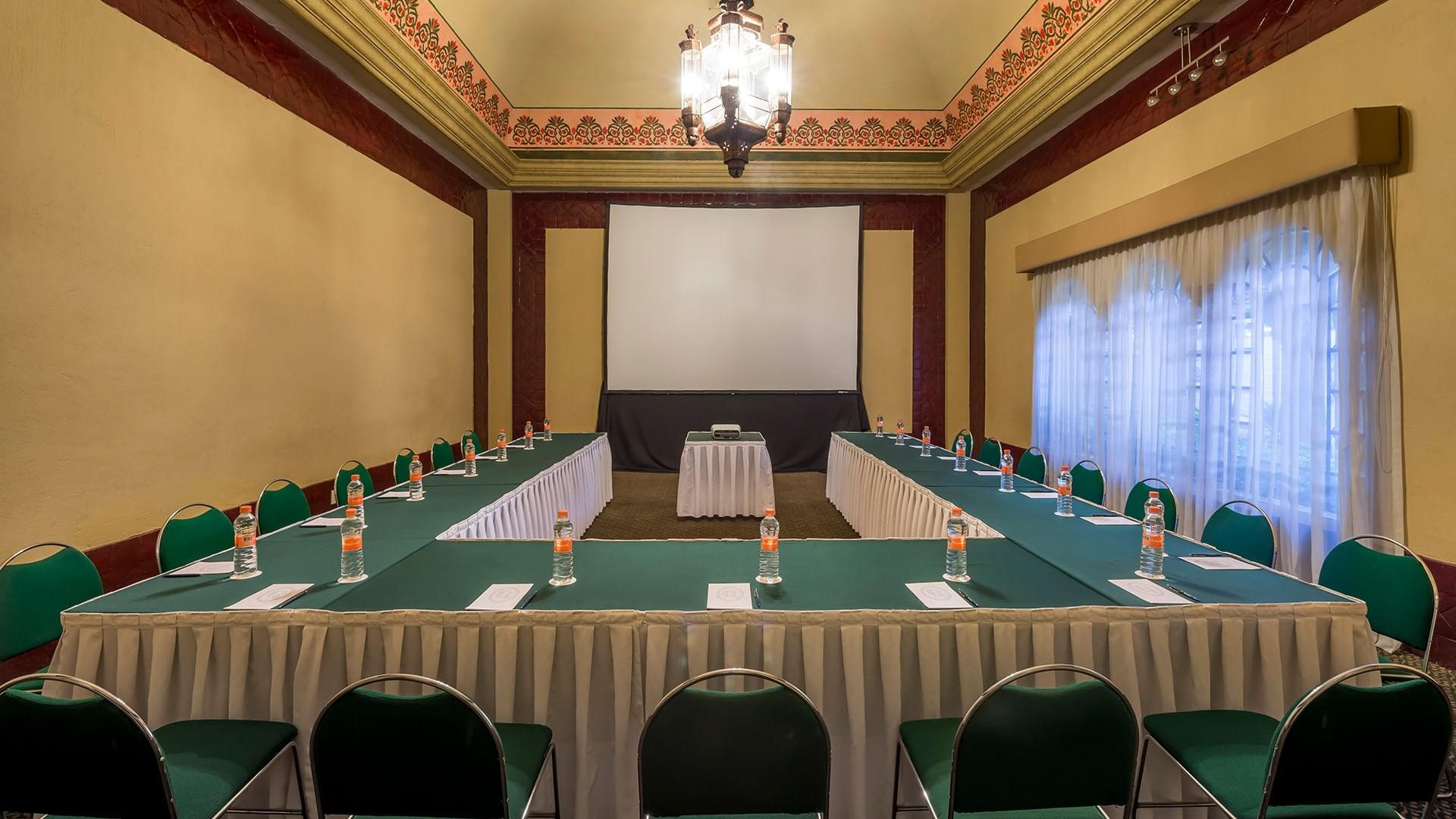Large U-shaped Salón Marqués featuring green chairs and white linens with water bottels at Quinta Real Aguascalientes