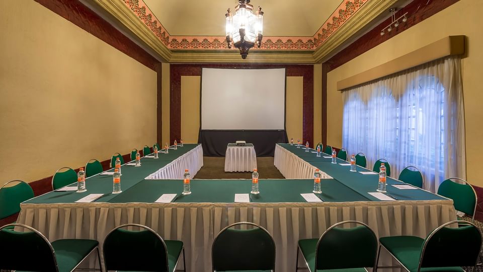Large U-shaped Salón Marqués featuring green chairs and white linens with water bottels at Quinta Real Aguascalientes