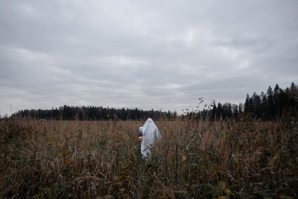 A person dressed in a ghost costume walking through a dark, empty field.