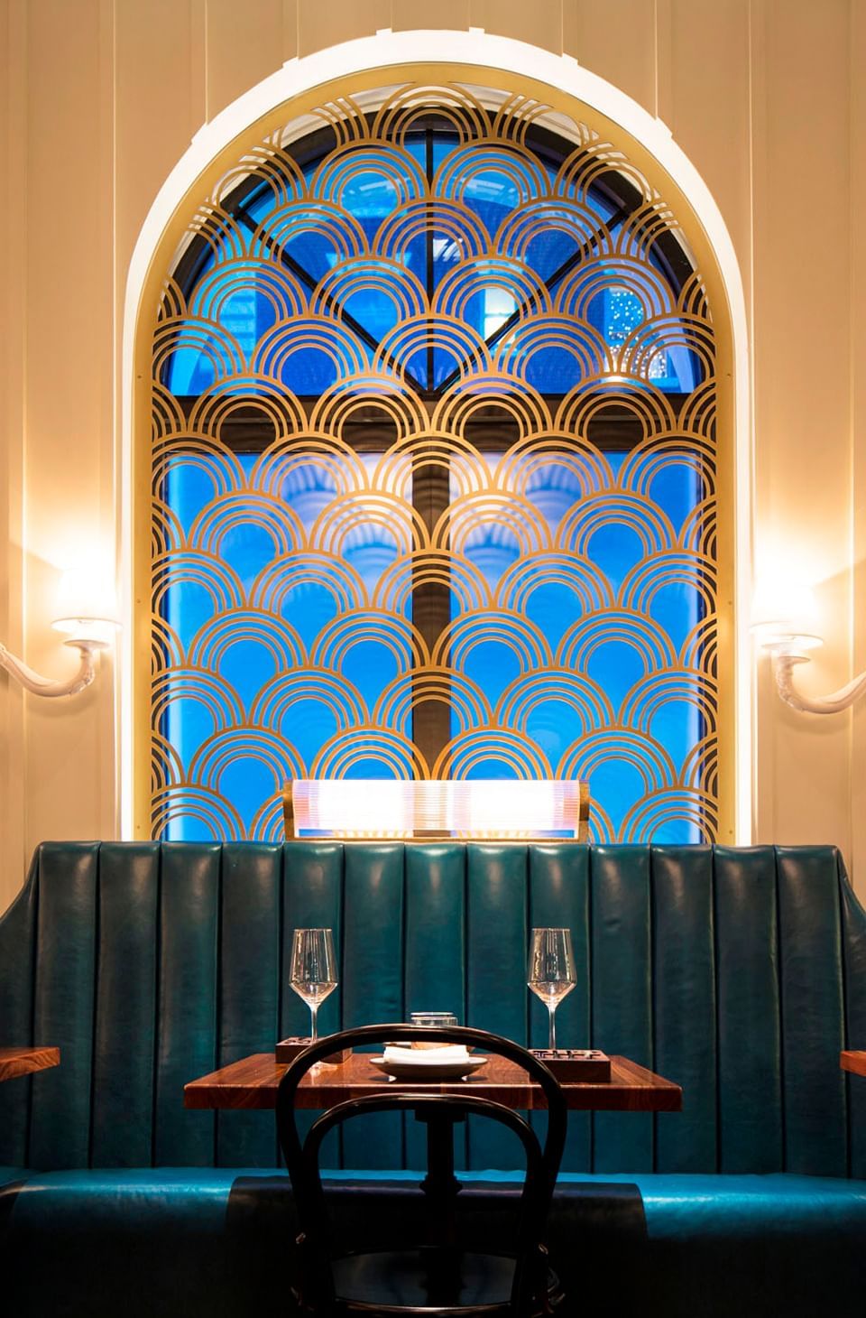 Ciaorigato Restaurant interior with a gold-patterned arch window, teal booths, and dining tables at Hotel Bijou