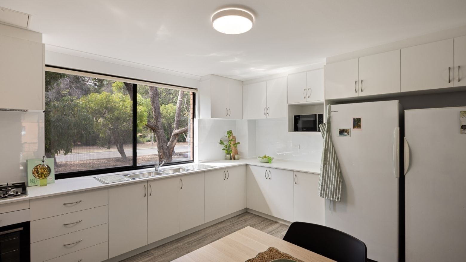 Modern white kitchen with appliances and dining area at UniLodge at Curtin University - Erica Underwood House.