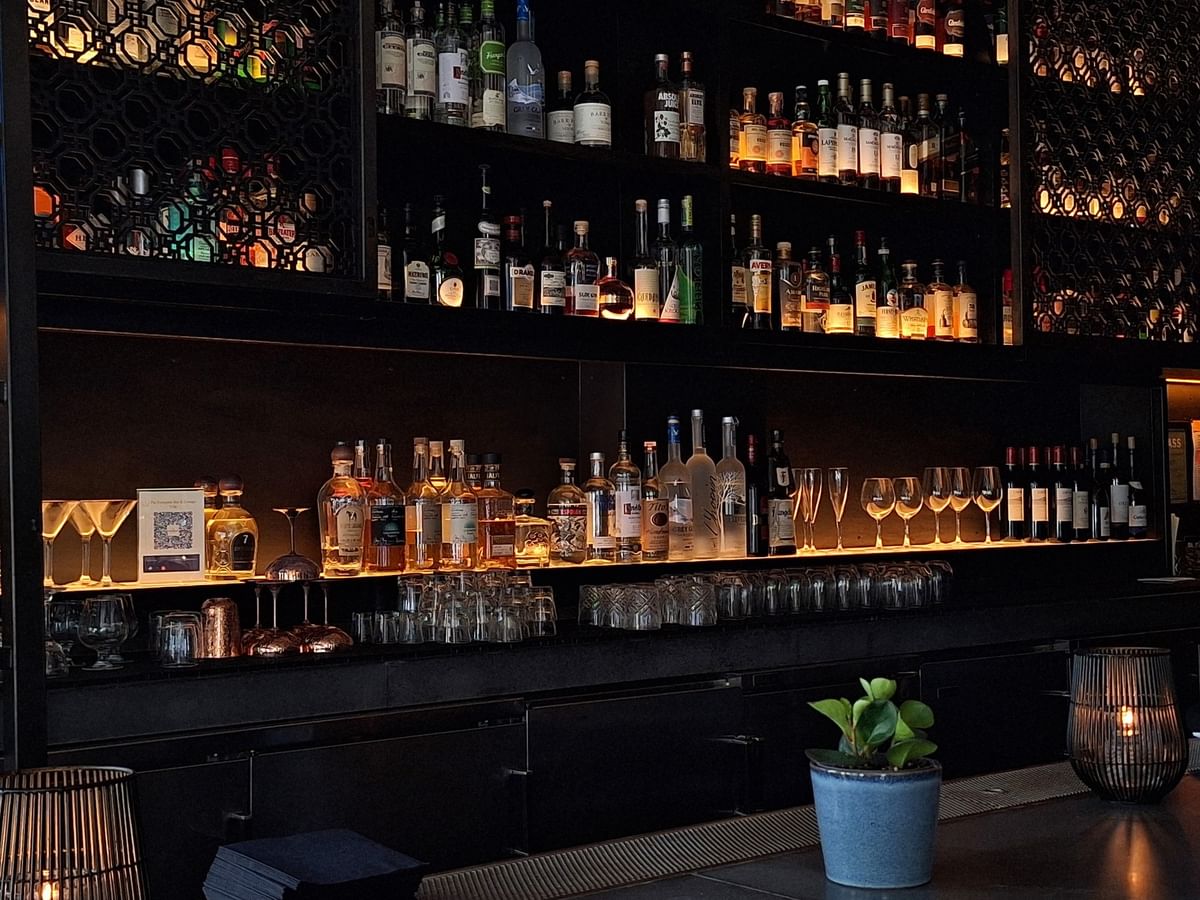 Liquor bottles on backlit shelves by rows of wine glasses under a dark ceiling at Warwick San Francisco