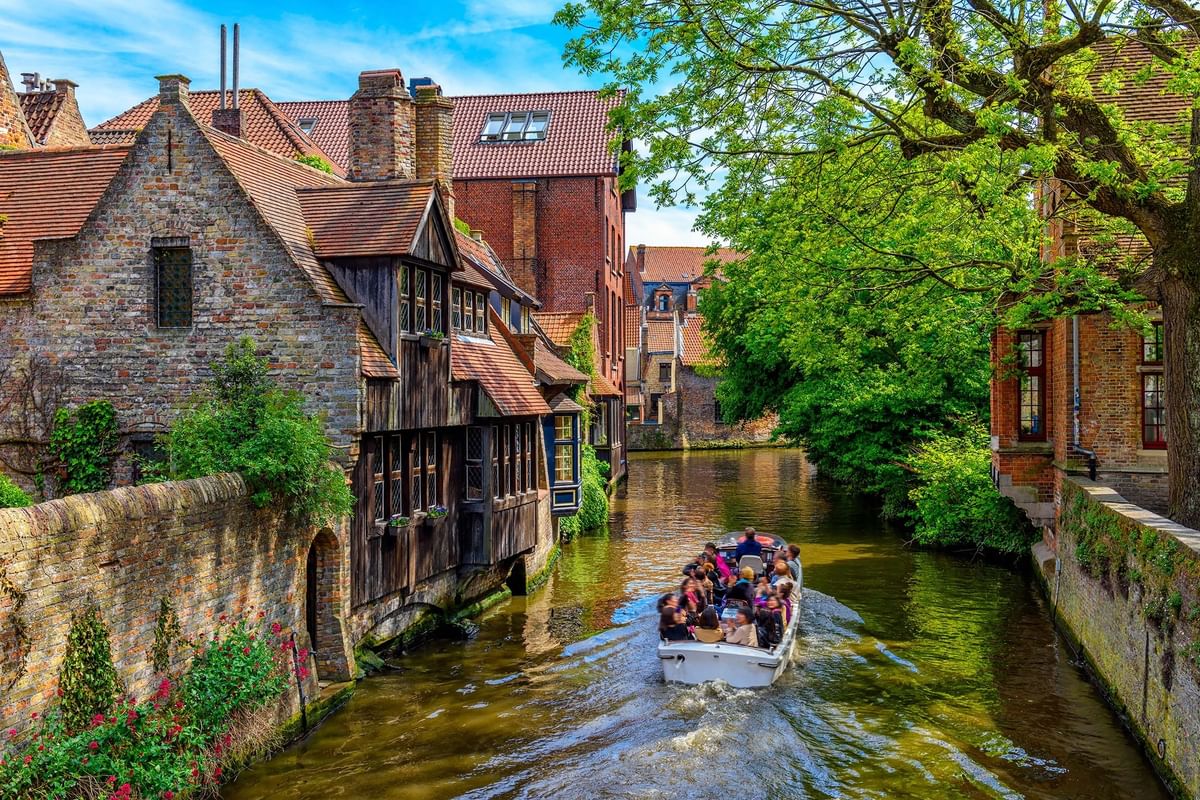 Boat tour with passengers sailing canal by brick houses at Bruges Canals near Warwick Grand Place Brussels