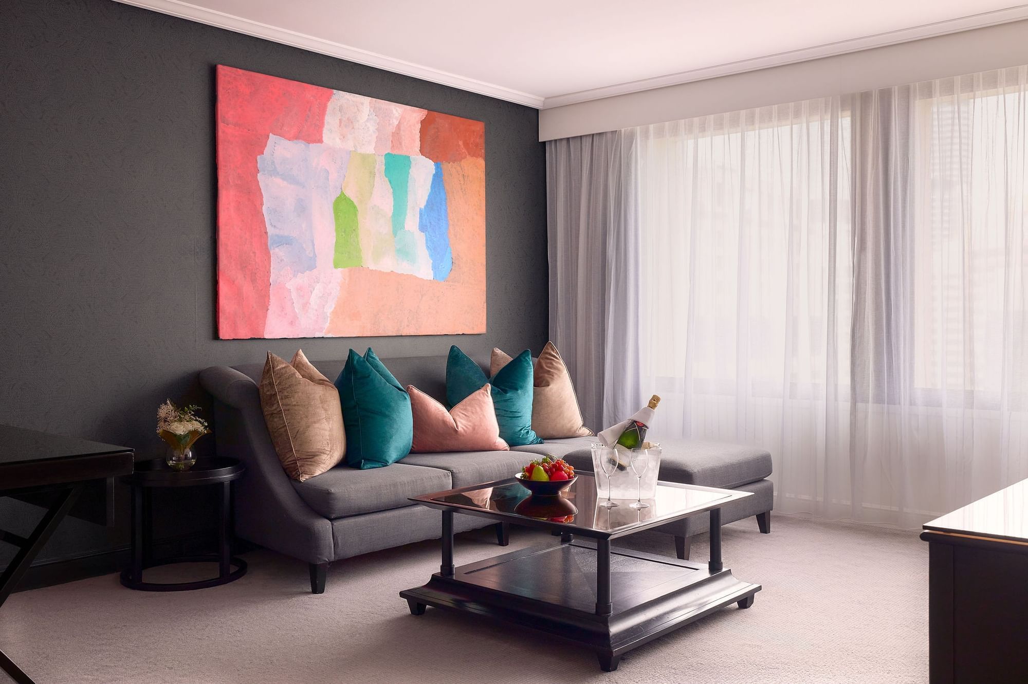 Living room with a sofa, colorful pillows, abstract art, & champagne bottle at Sofitel Brisbane Central