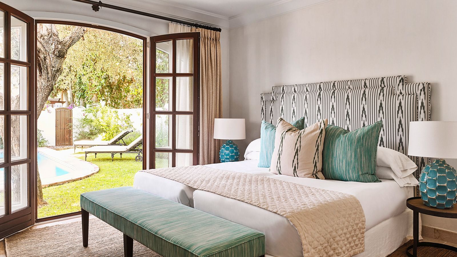 Bedroom with an ikat headboard and bench by French doors that open to a garden at the Marbella Club