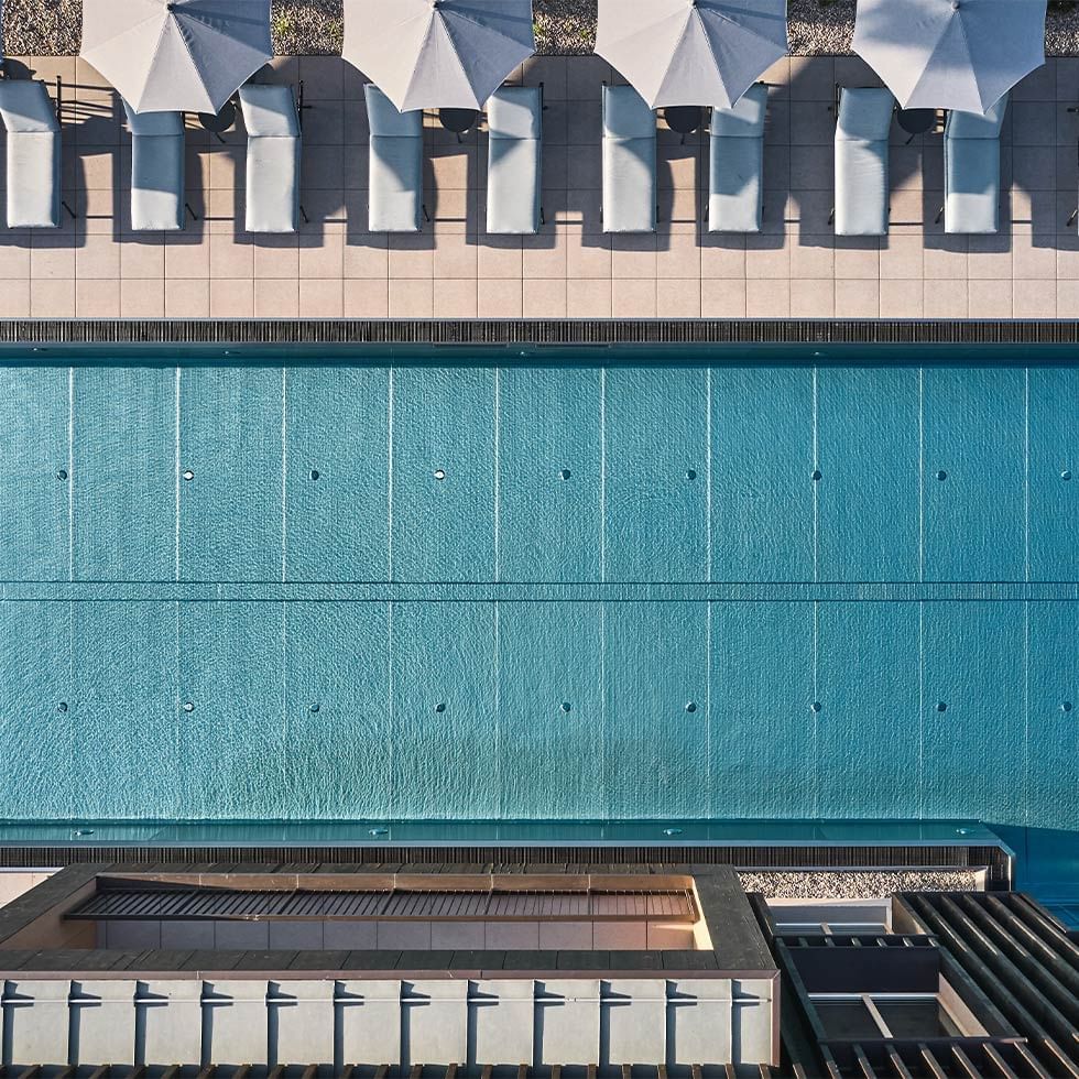 An aerial view of a swimming pool with lounge chairs and umbrellas around its edge.