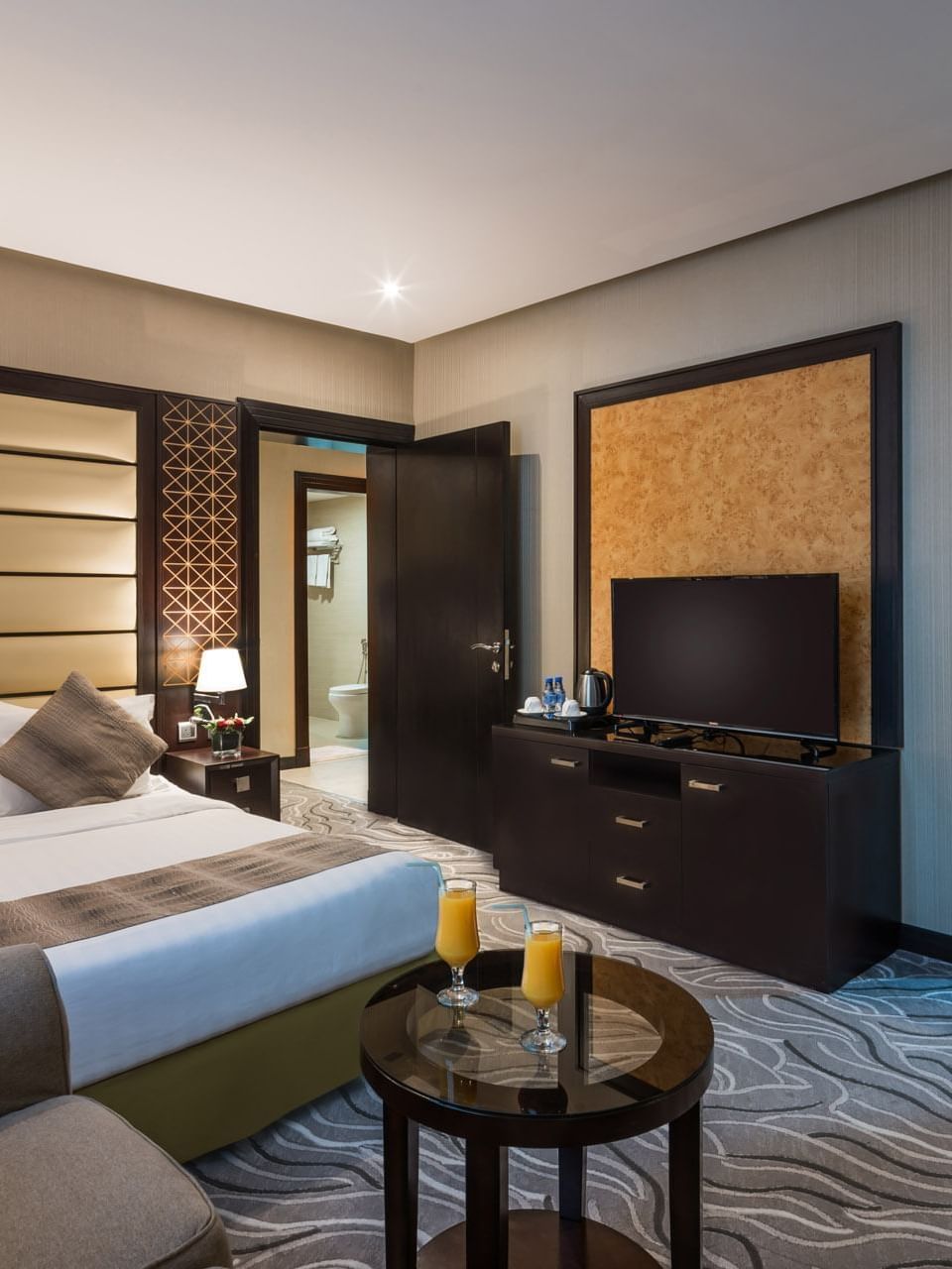 Large bed by a TV stand under a patterned wall with an open door in Executive Suite at Naviti by Warwick Al Khobar