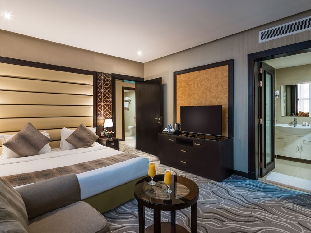 Large bed by a TV stand under a patterned wall with an open door in Executive Suite at Naviti by Warwick Al Khobar