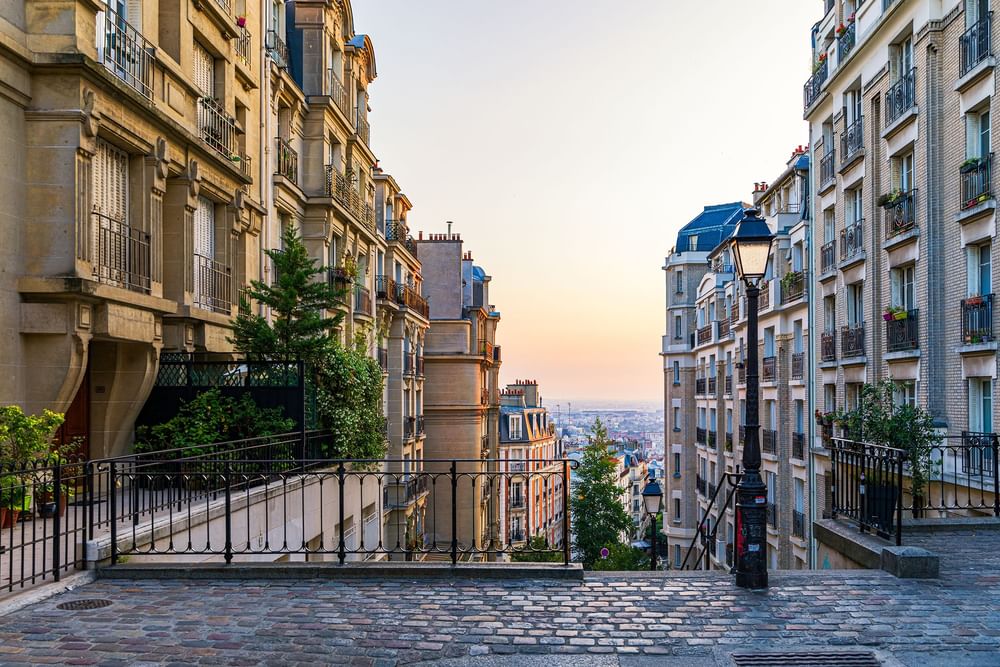 Cobblestone path by iron rails under a soft sunset, surrounding flats near Warwick Paris Champs Elysées