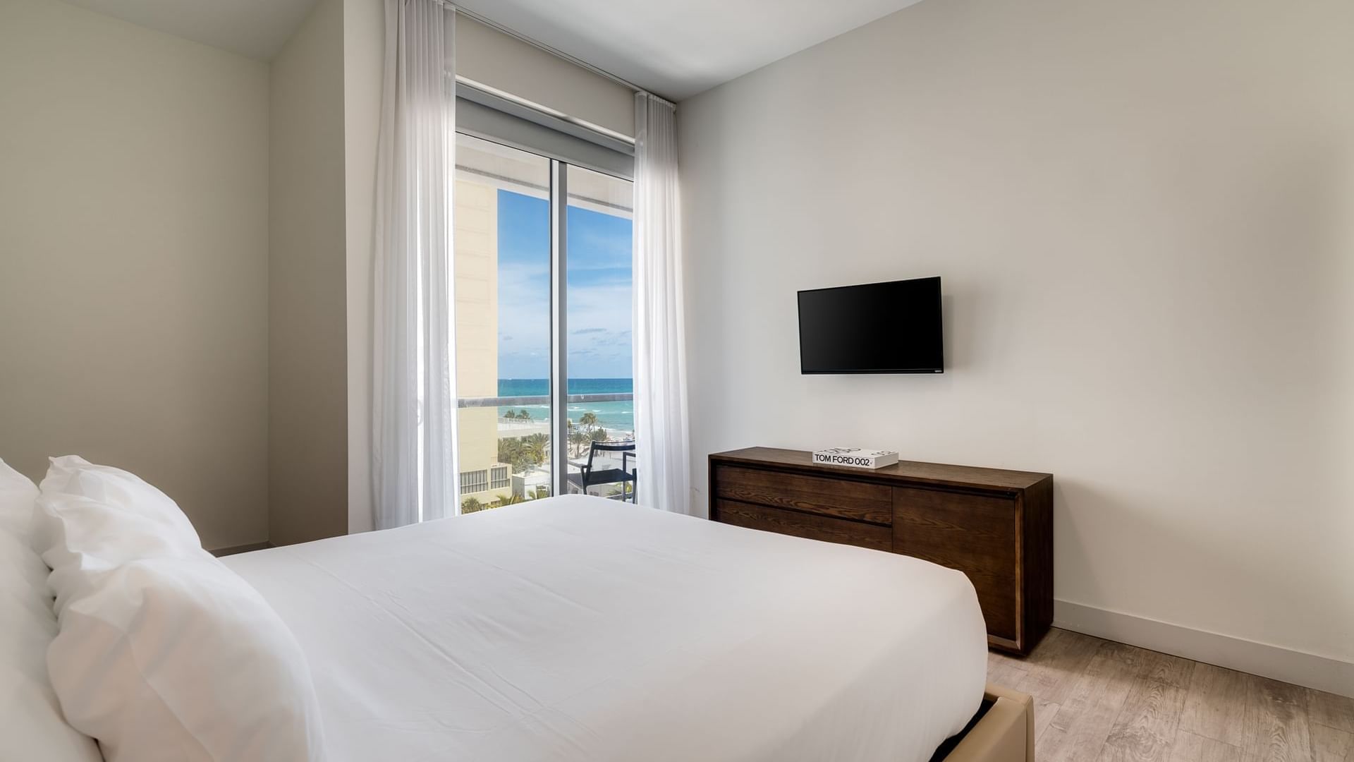 A hotel room with a bed, dresser, TV, and window with a view.