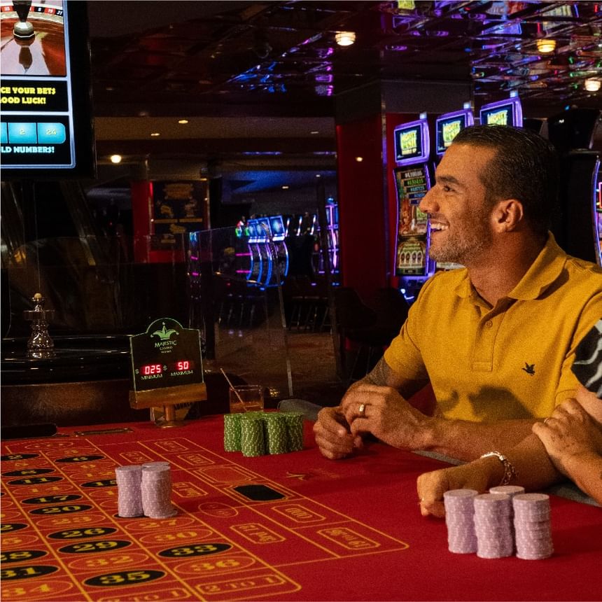 Hombre sonriente sentado junto a una mesa de ruleta con fichas bajo luz ambiental en Megapolis Hotel Panama